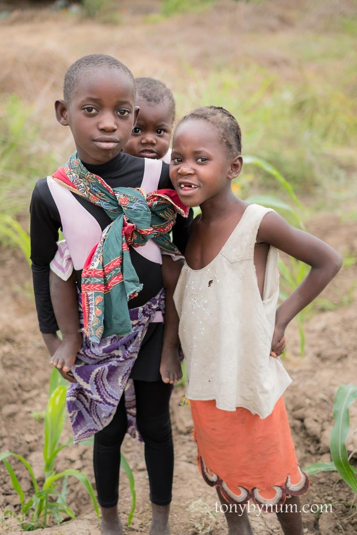 Three children standing in a field with one child carrying a baby.